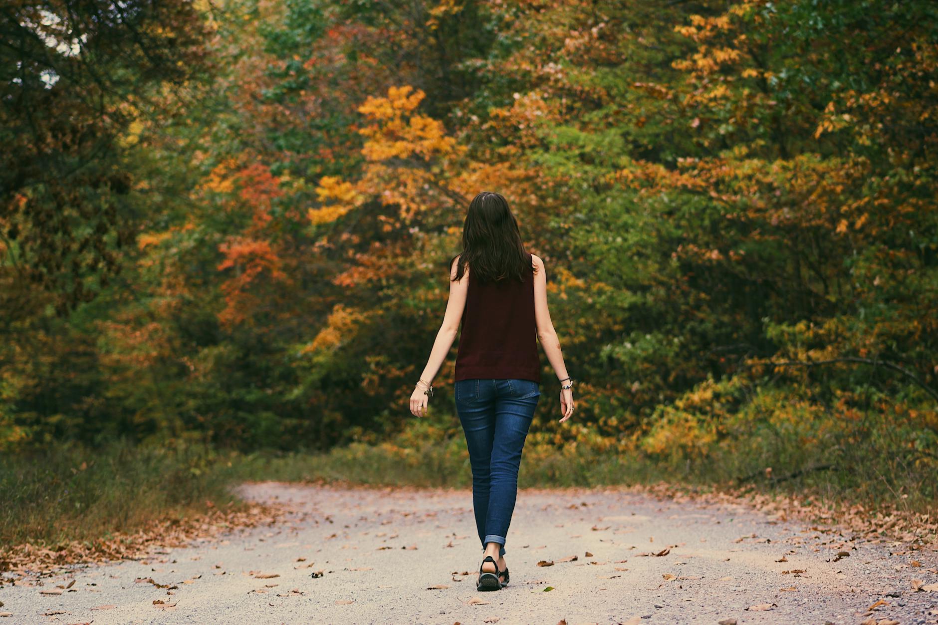 woman in brown sleeveless dress and blue jeans standing on gray path road